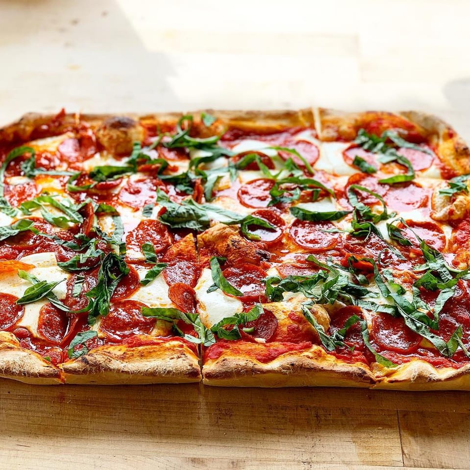 Mikey's Pizza rectangular pepperoni pizza with fresh basil on a wooden surface.